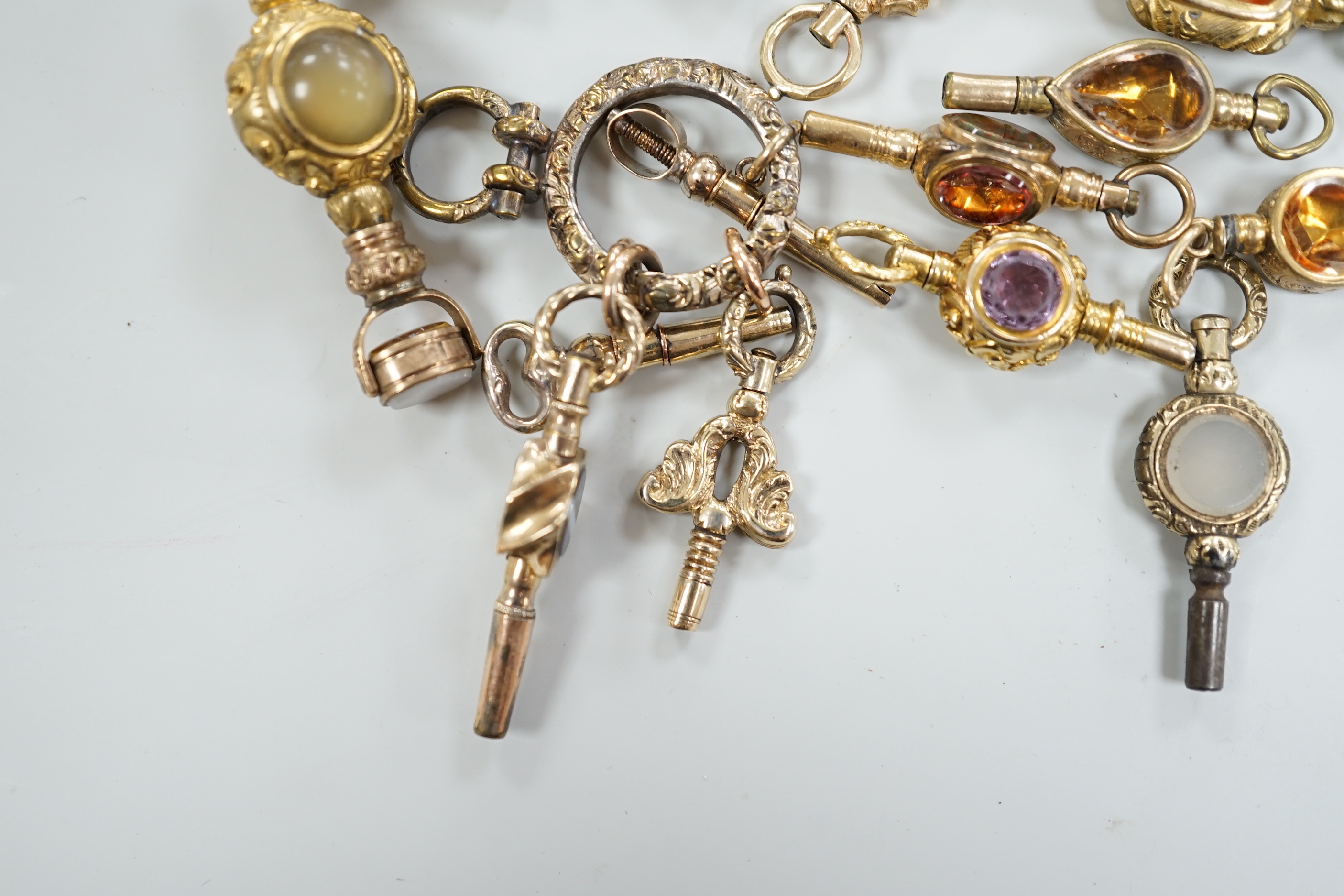 Sixteen assorted 19th century yellow metal overlaid and mainly gem set small watch keys, including chalcedony, citrine, amethyst, banded agate, bloodstone and a ring with four keys attached, largest 47mm.